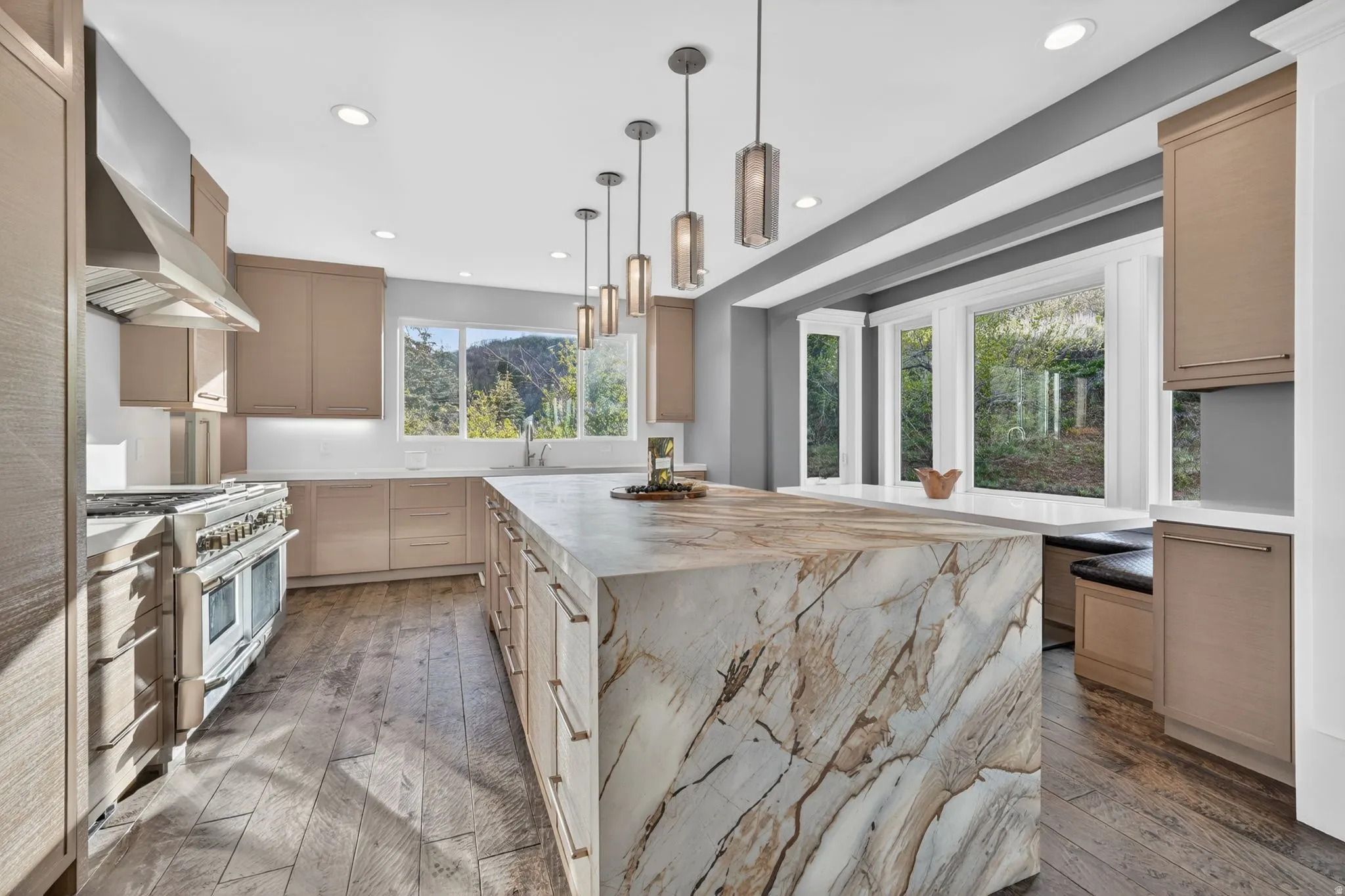 Kitchen with light wood finish cabinetry, a center island, light stone counters, and range with two ovens