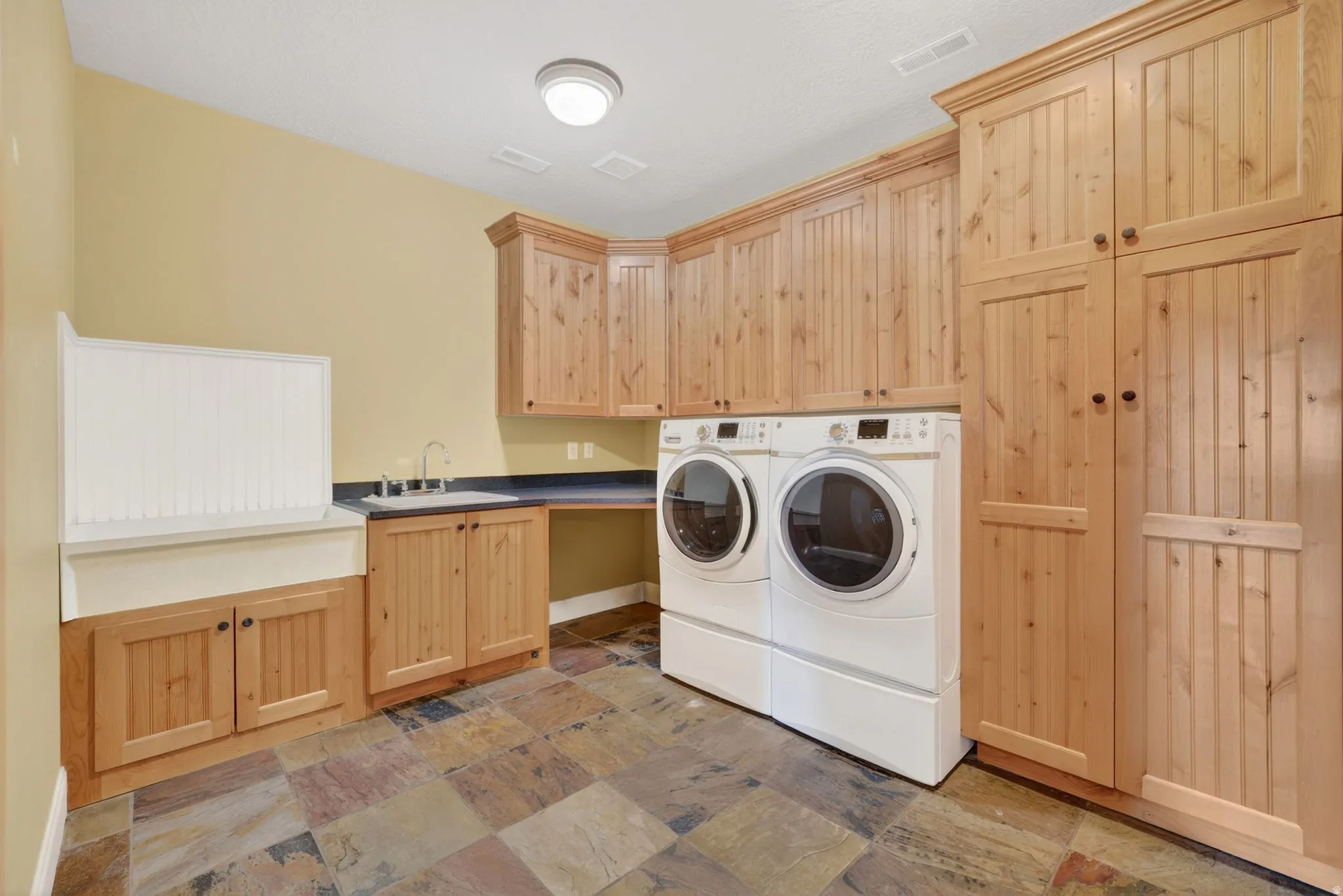 Laundry area featuring independent washer and dryer, light stone finish floors, and cabinet space