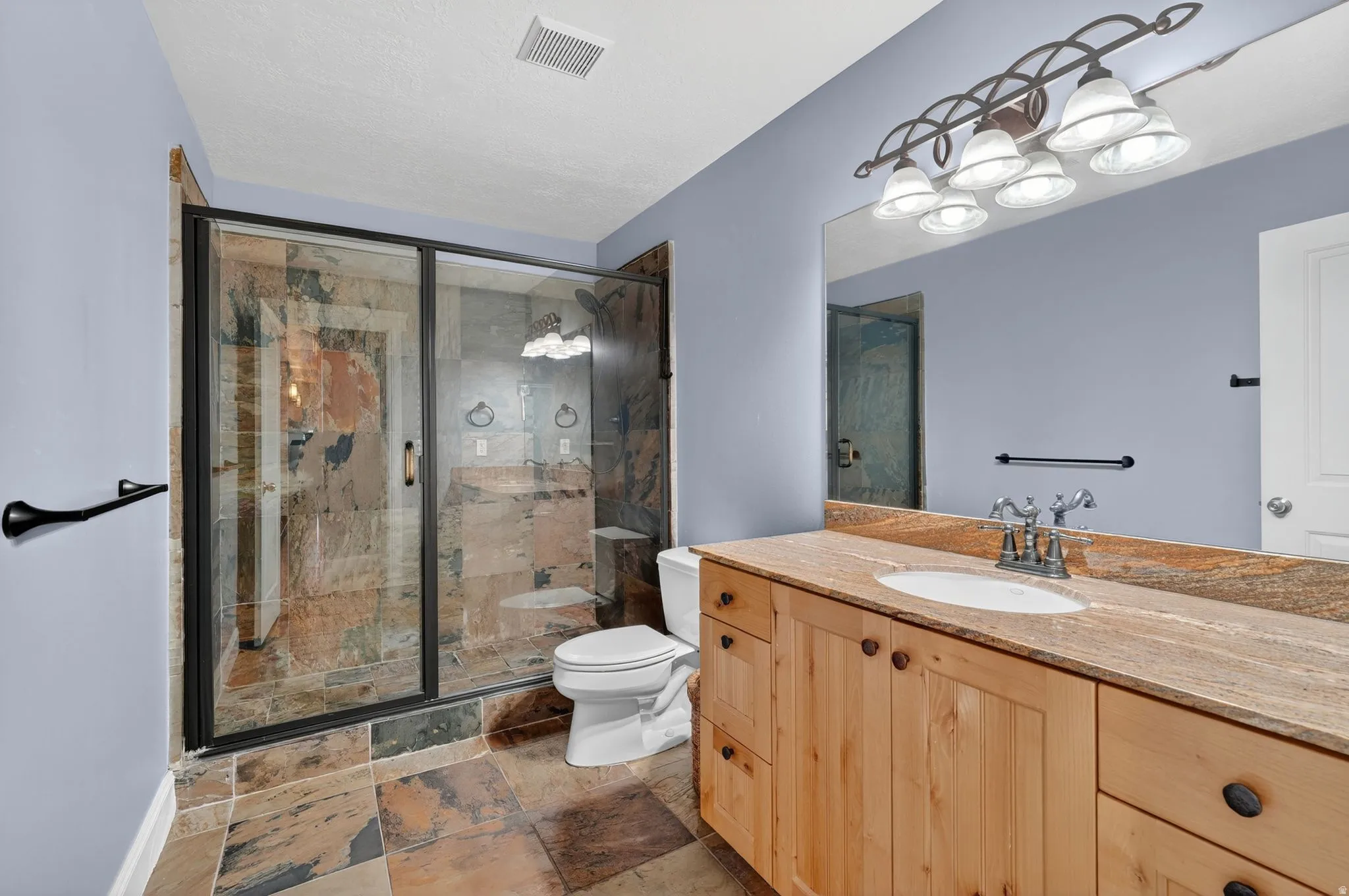 Bathroom with vanity, a marble finish shower, and stone tile floors