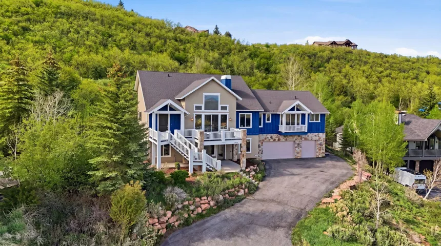 View of front of home with an attached garage, driveway, stone siding, a chimney, and a shingled roof
