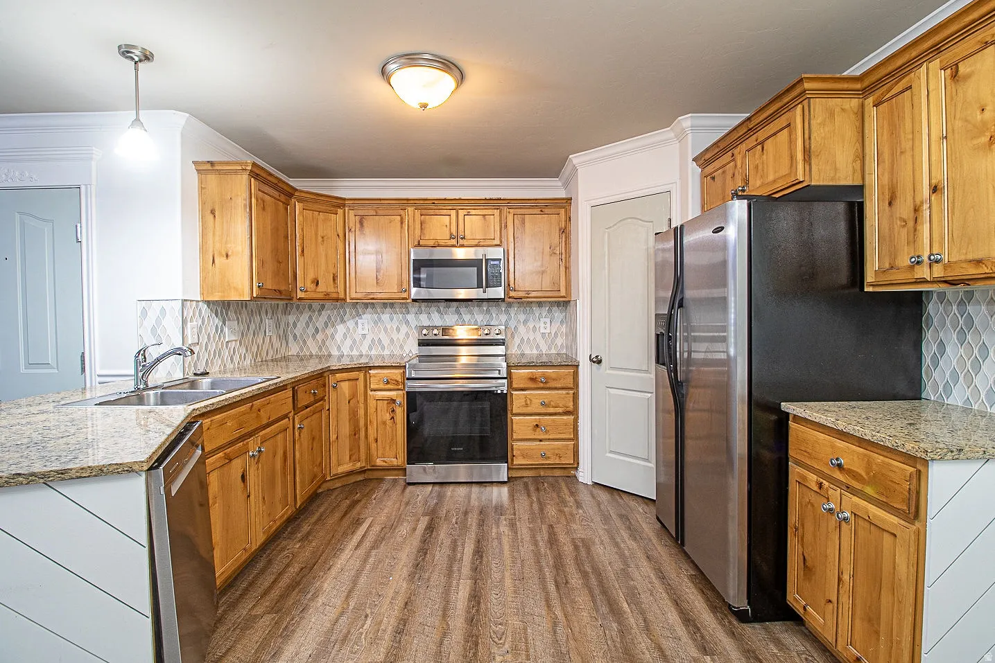 Kitchen with decorative backsplash, stainless steel appliances, wood finish cabinetry, dark wood-style flooring, and light stone countertops