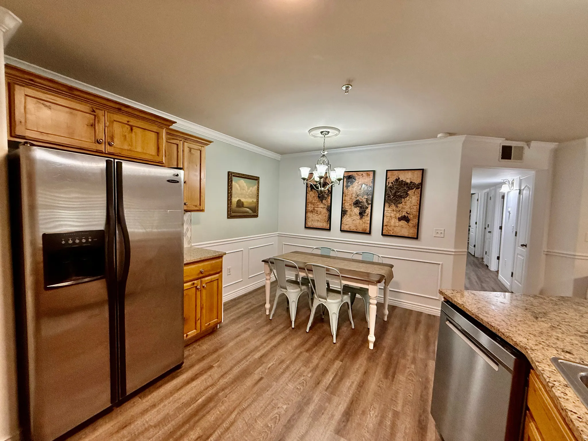 Kitchen featuring stainless steel appliances, crown molding, wood finish cabinetry, light wood-style flooring, and wainscoting