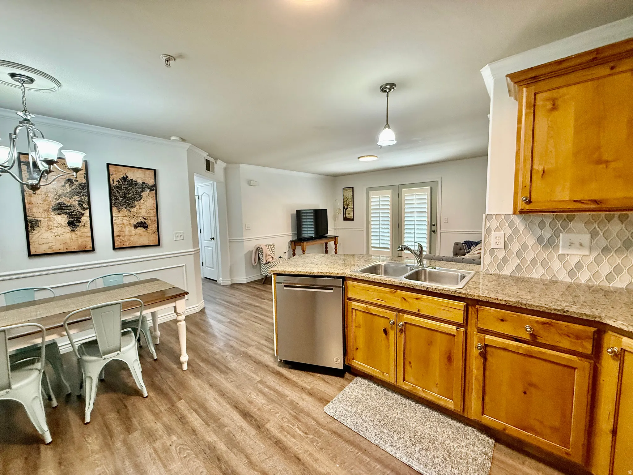 Kitchen with stainless steel dishwasher, a peninsula, crown molding, light wood-type flooring, and hanging lights