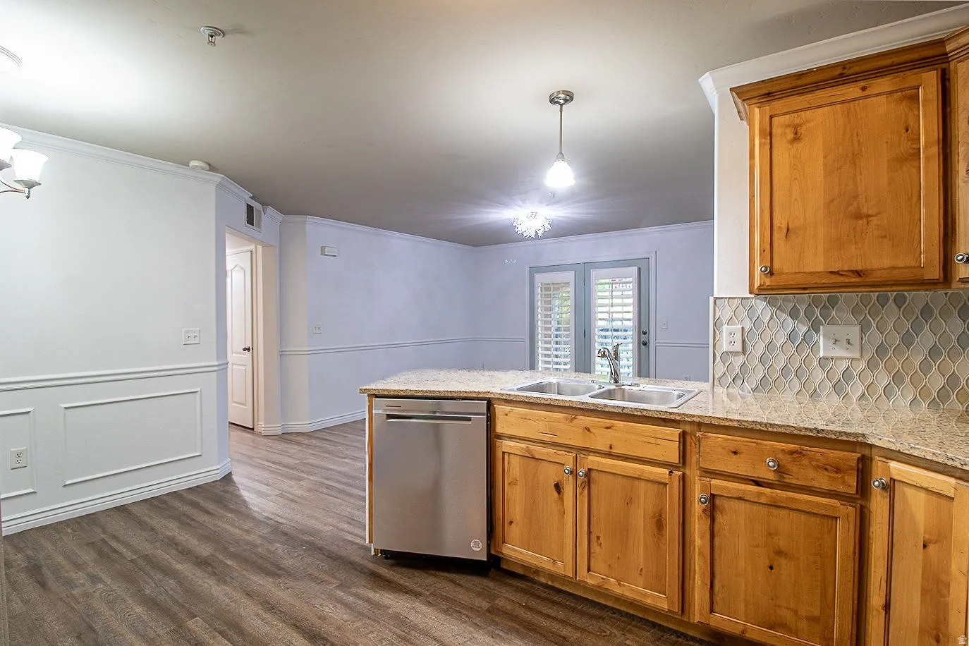 Kitchen featuring a peninsula, a chandelier, dishwasher, light stone counters, and dark wood-type flooring