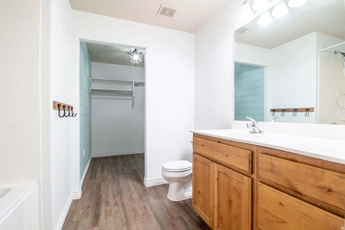 Full bath with vanity, dark wood finished floors, a walk in closet, and a tub