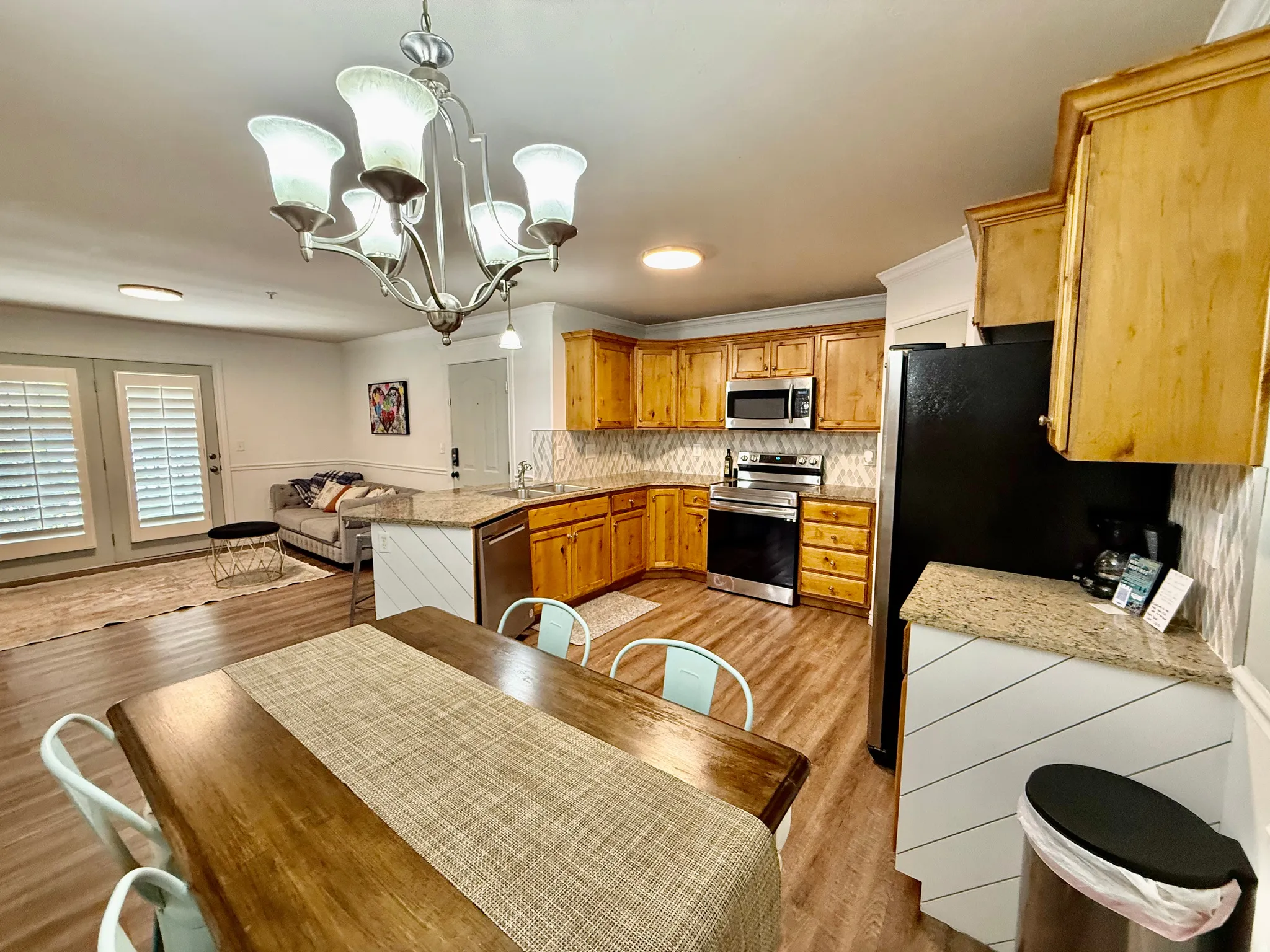 Kitchen with a peninsula, stainless steel appliances, hanging lights, light wood-style flooring, and light stone countertops