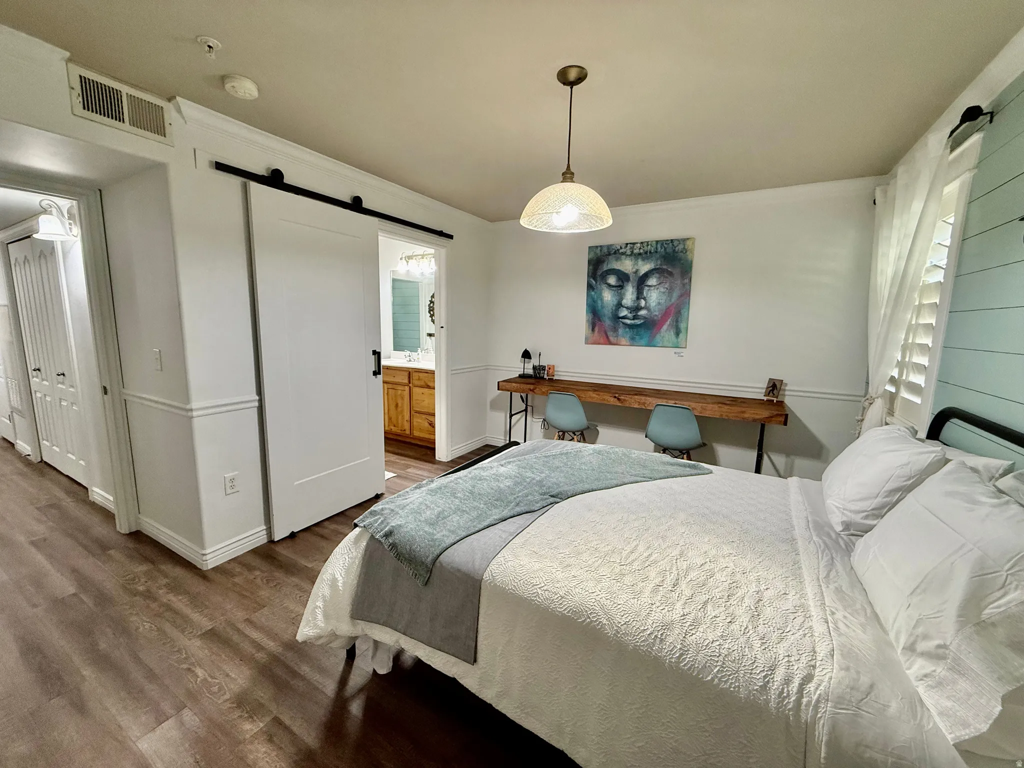 Bedroom featuring a barn door, dark wood-style flooring, ornamental molding, and connected bathroom