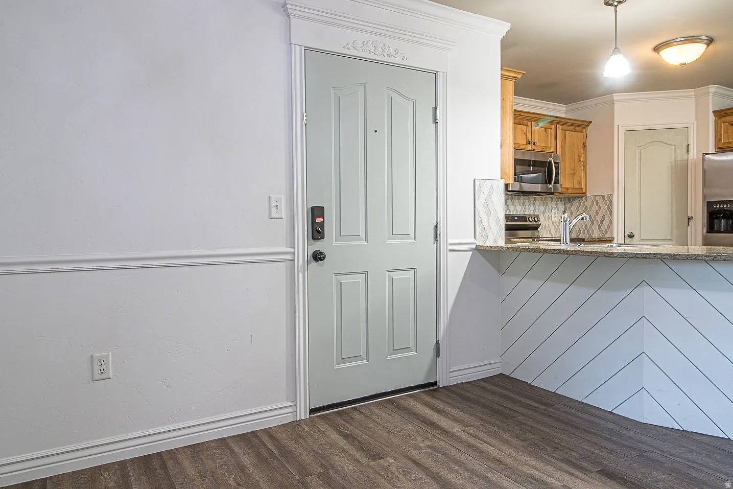Kitchen featuring dark wood-type flooring, tasteful backsplash, stainless steel appliances, light stone counters, and wood finish cabinets