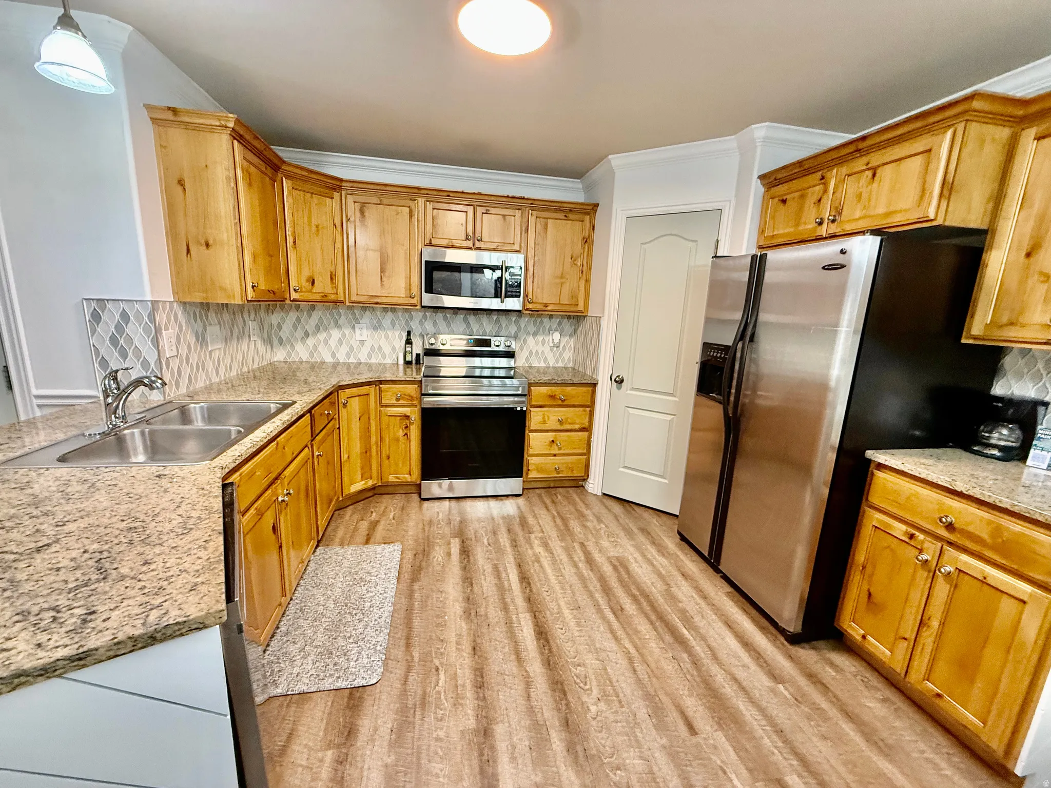 Kitchen with stainless steel appliances, light wood finished floors, backsplash, light stone counters, and ornamental molding