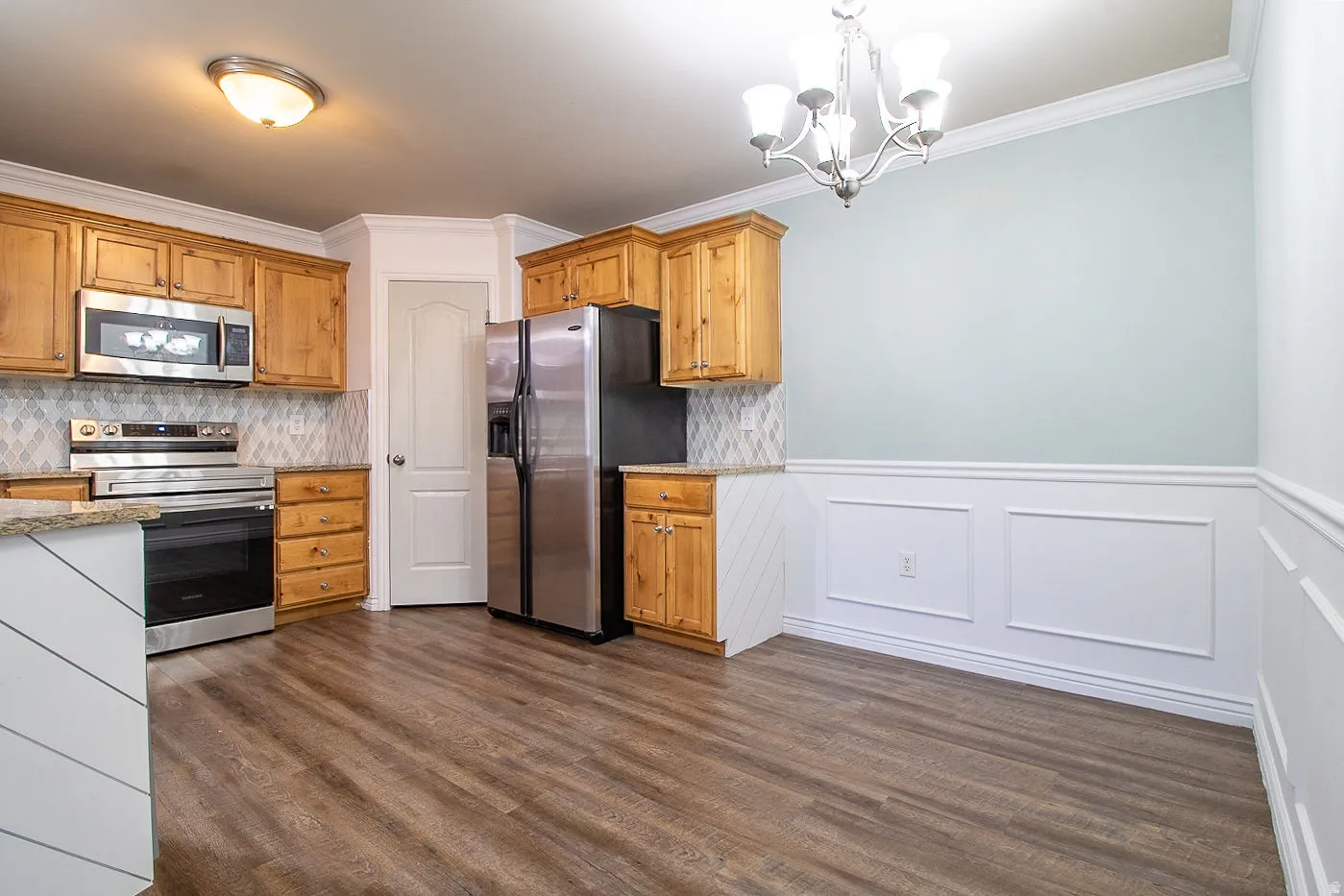 Kitchen featuring stainless steel appliances, hanging lights, light stone countertops, crown molding, and wainscoting