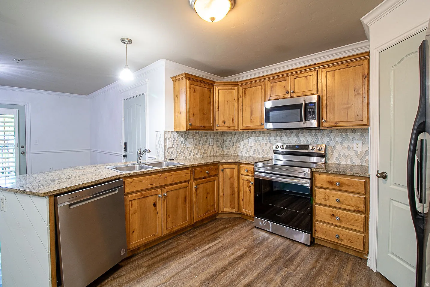 Kitchen featuring stainless steel appliances, a peninsula, ornamental molding, dark wood-style flooring, and wood finish cabinetry