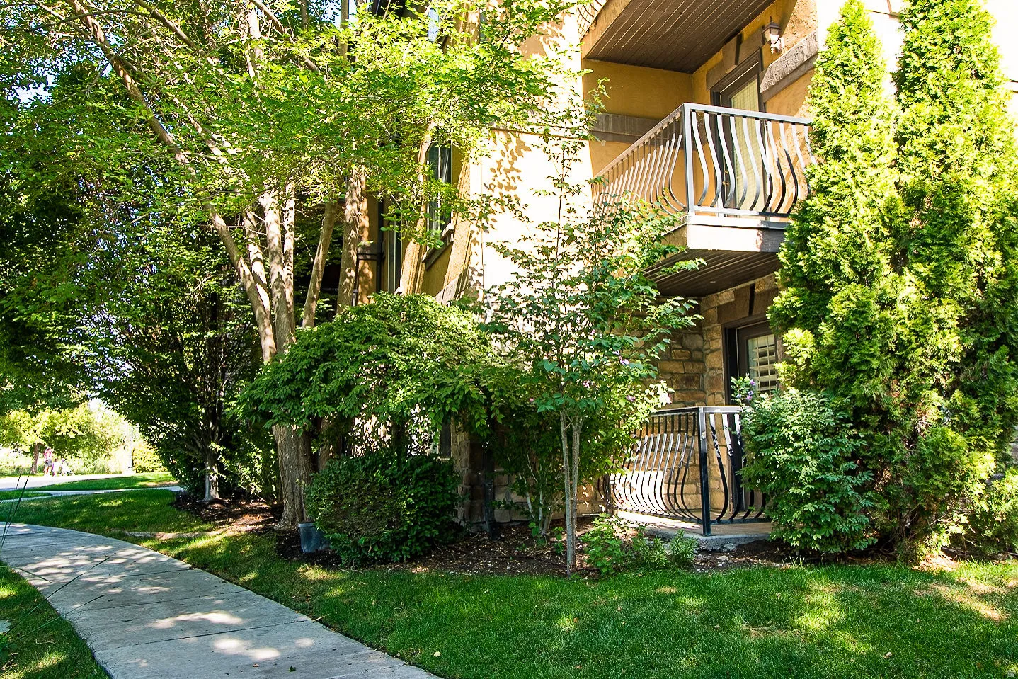 View of side of property with a balcony, a yard, stucco siding, and stone siding