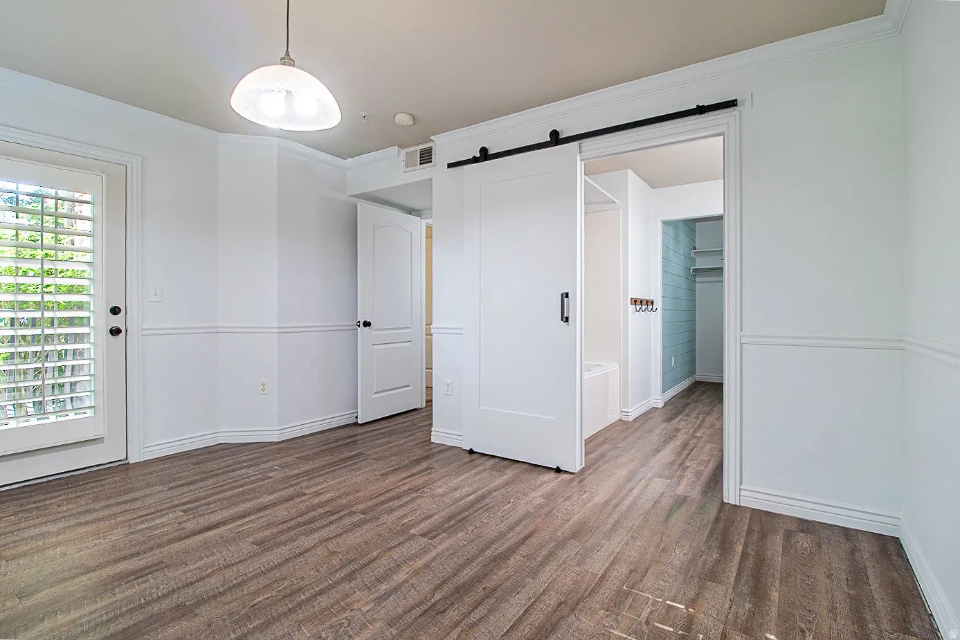 Unfurnished bedroom featuring a barn door, dark wood-style flooring, crown molding, and a spacious closet