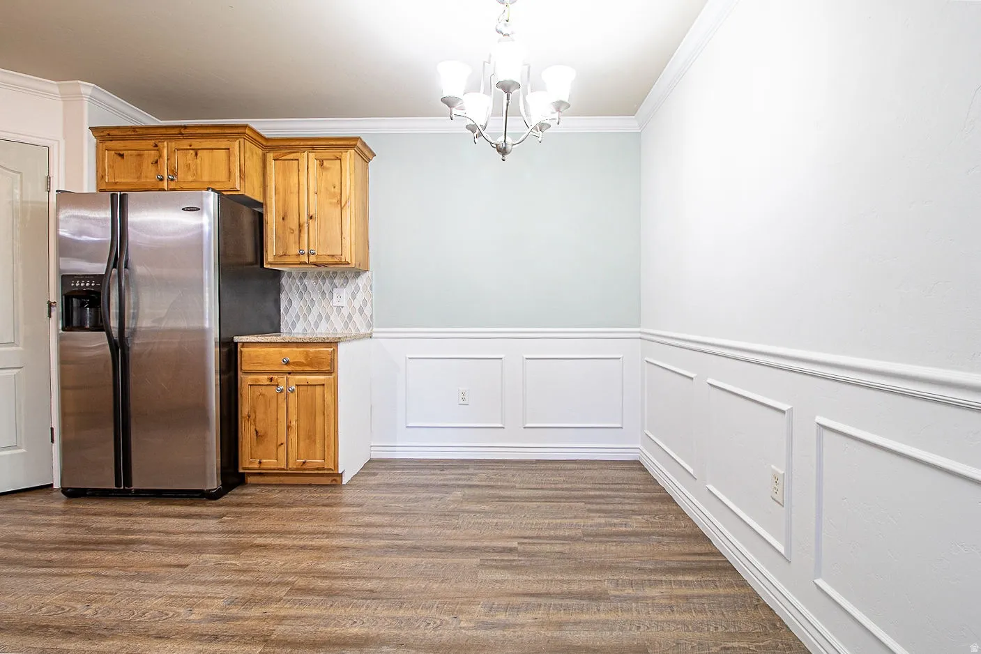 Kitchen with stainless steel fridge with ice dispenser, wood finish cabinets, a chandelier, crown molding, and dark wood-type flooring