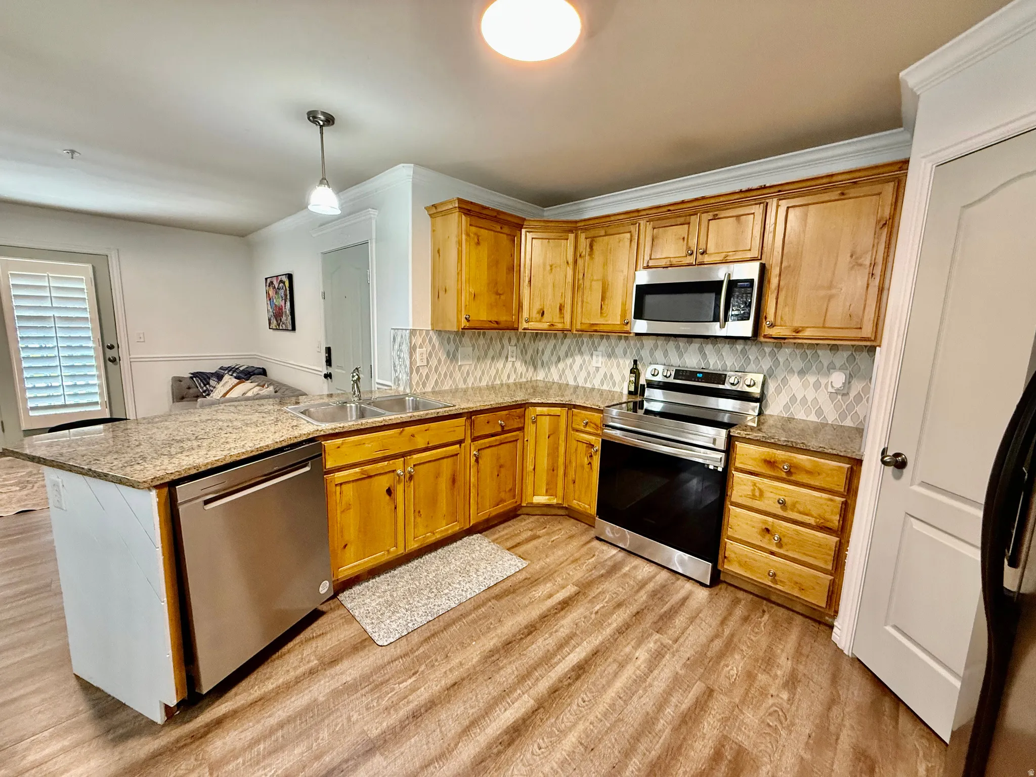 Kitchen featuring stainless steel appliances, a peninsula, light wood-type flooring, decorative light fixtures, and ornamental molding