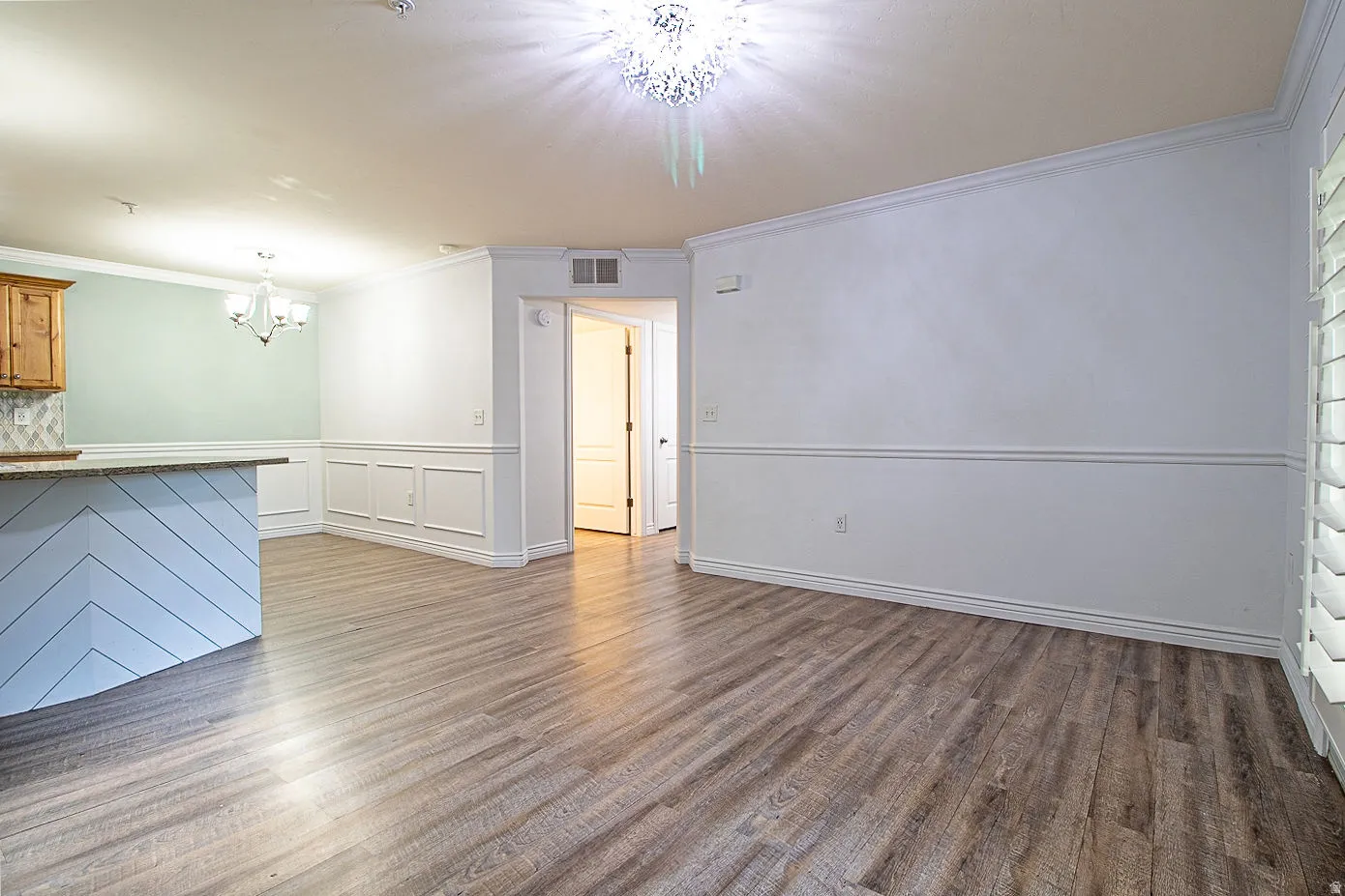 Unfurnished living room featuring a chandelier, ornamental molding, dark wood-style floors, a wainscoted wall, and a decorative wall