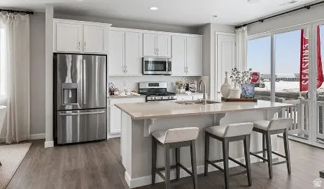 Kitchen with white cabinetry, stainless steel appliances, a kitchen breakfast bar, dark wood-style flooring, and recessed lighting.  This is a rendering photo only. Actual home may have different finishes and features than those shown.
