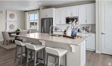 Kitchen featuring white cabinets, an island with sink, stainless steel appliances, a kitchen breakfast bar, and recessed lighting.  This is a rendering photo only. Actual home may have different finishes and features than those shown.