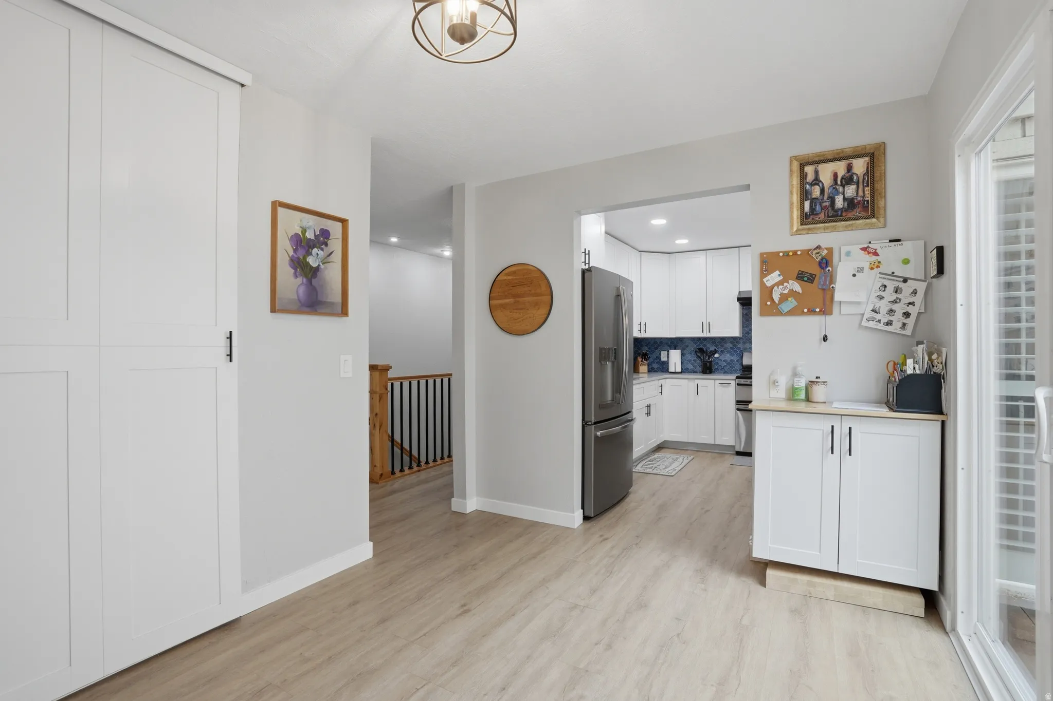 Kitchen with light countertops, white cabinetry, stainless steel fridge, light wood-style flooring, and decorative backsplash