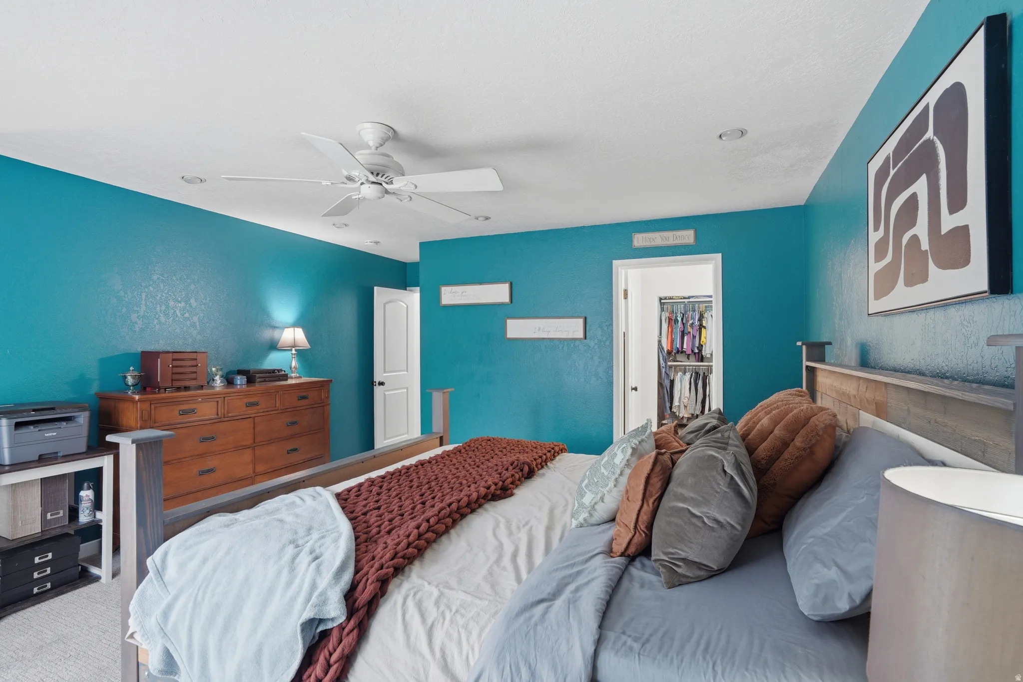 Carpeted bedroom with a spacious closet, a ceiling fan, and a textured wall