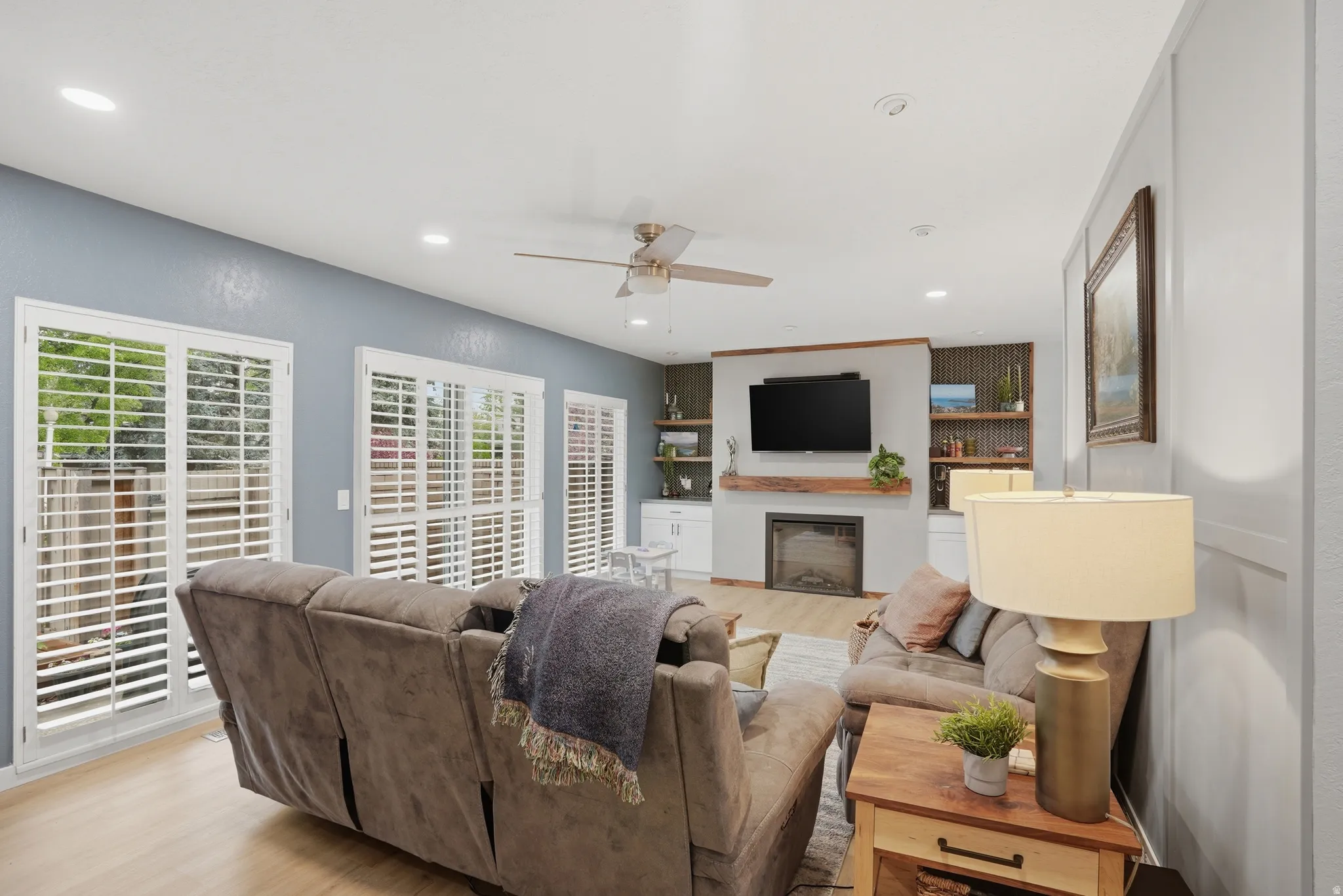Living room featuring light wood-style flooring, ceiling fan, recessed lighting, and a fireplace