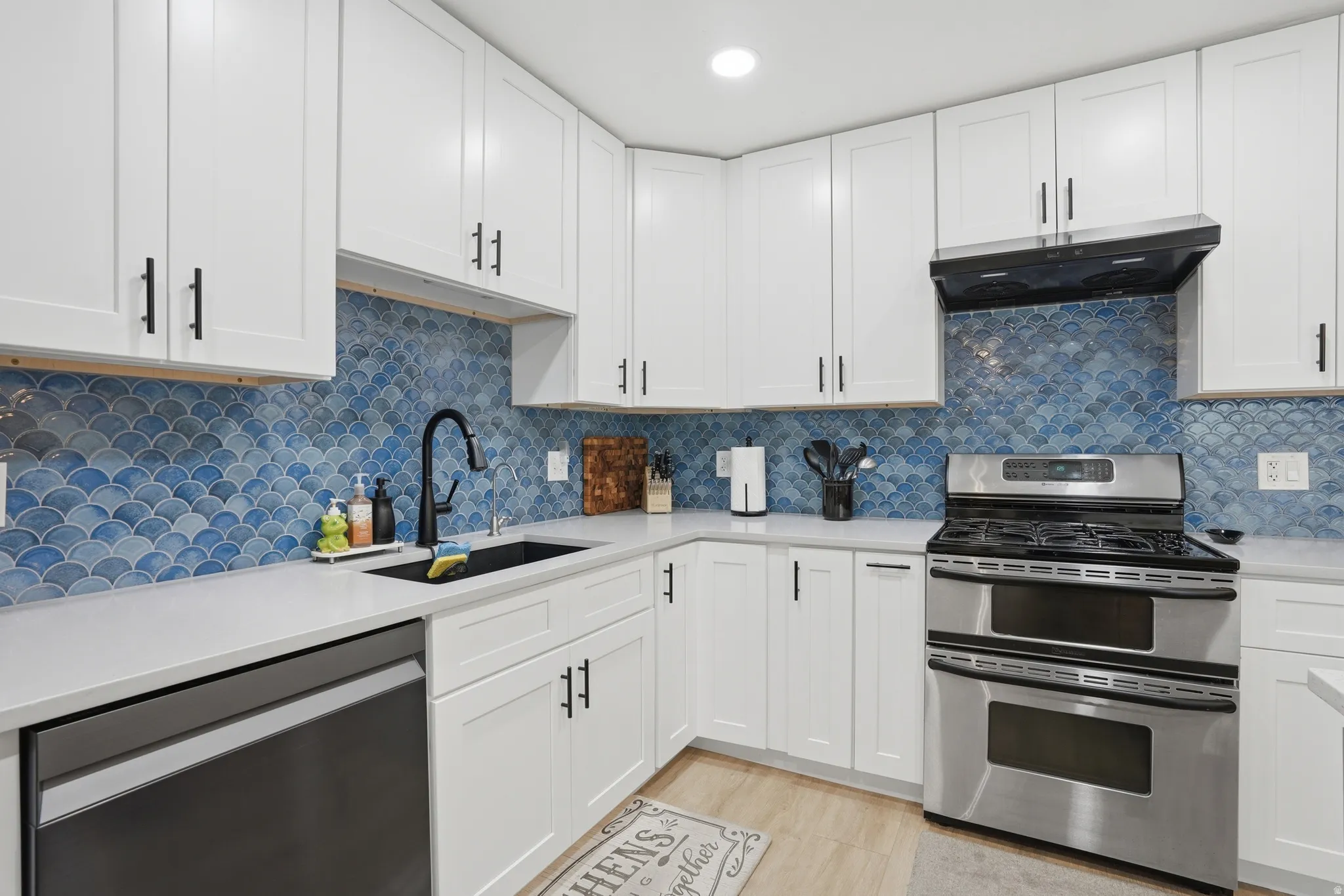 Kitchen featuring stainless steel appliances, white cabinets, light stone countertops, backsplash, and recessed lighting