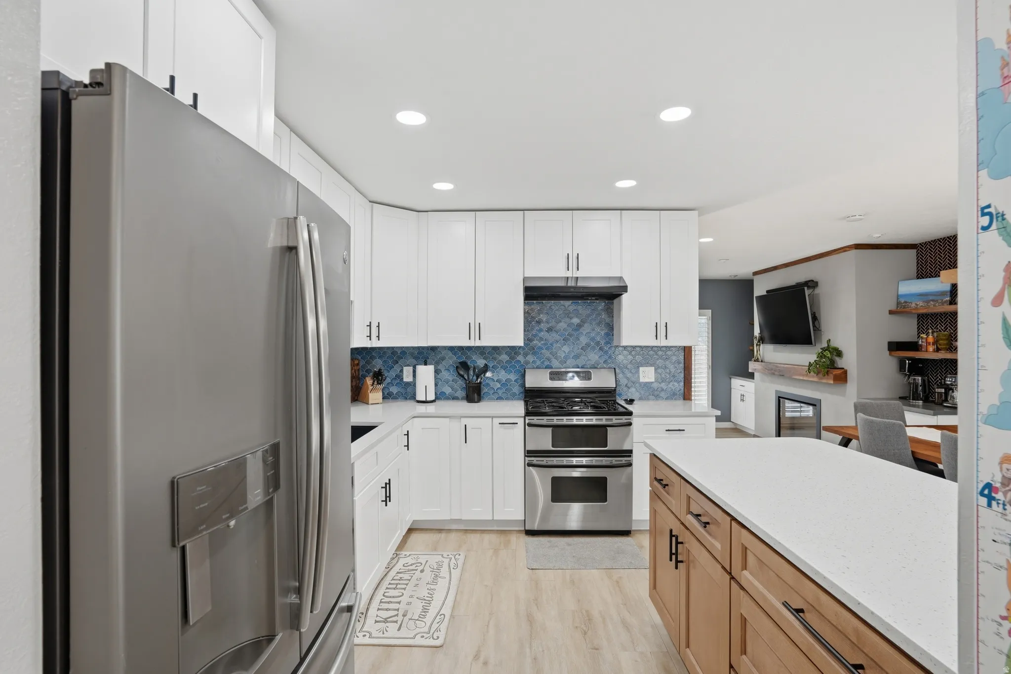 Two tone kitchen with stainless steel appliances, two tone color scheme, light wood finished floors, light stone counters, and recessed lighting