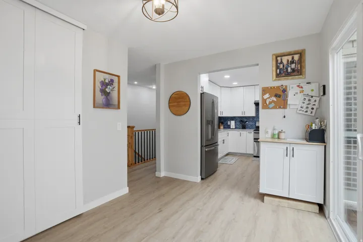 Kitchen with light countertops, white cabinetry, stainless steel fridge, light wood-style flooring, and decorative backsplash