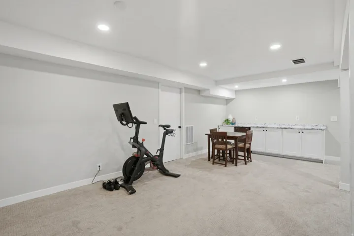 Exercise area with light carpet, recessed lighting, and wet bar