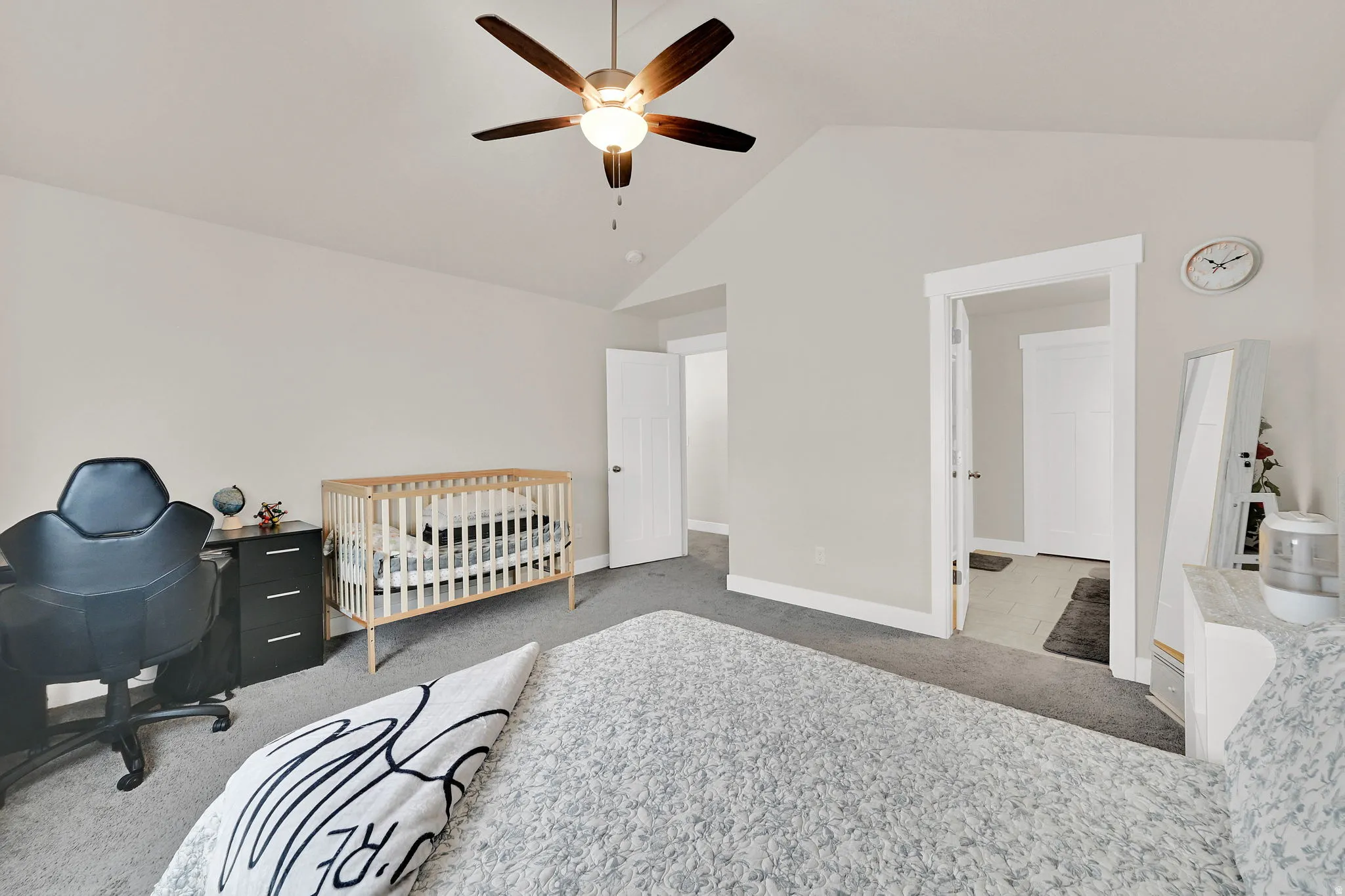 Bedroom with a crib, light carpet, a ceiling fan, and an office area