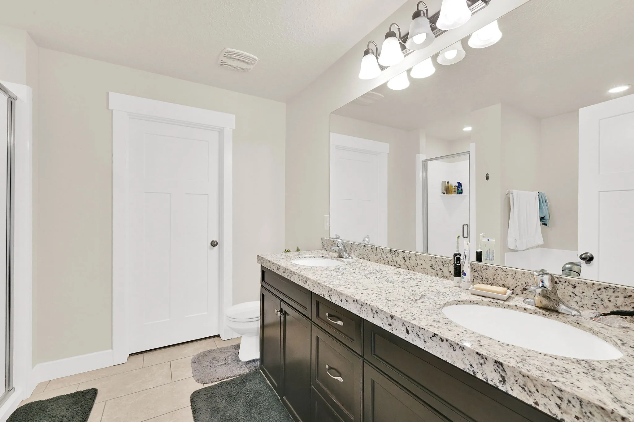 Full bath featuring double vanity, a shower stall, and light tile patterned floors