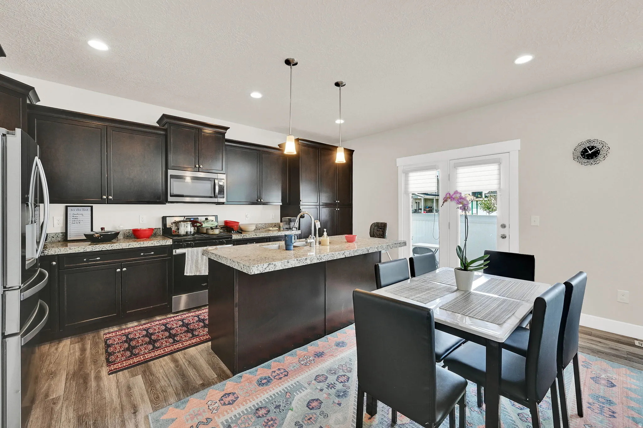 Kitchen with stainless steel appliances, dark wood-style flooring, a kitchen island with sink, hanging light fixtures, and dark wood finish cabinetry