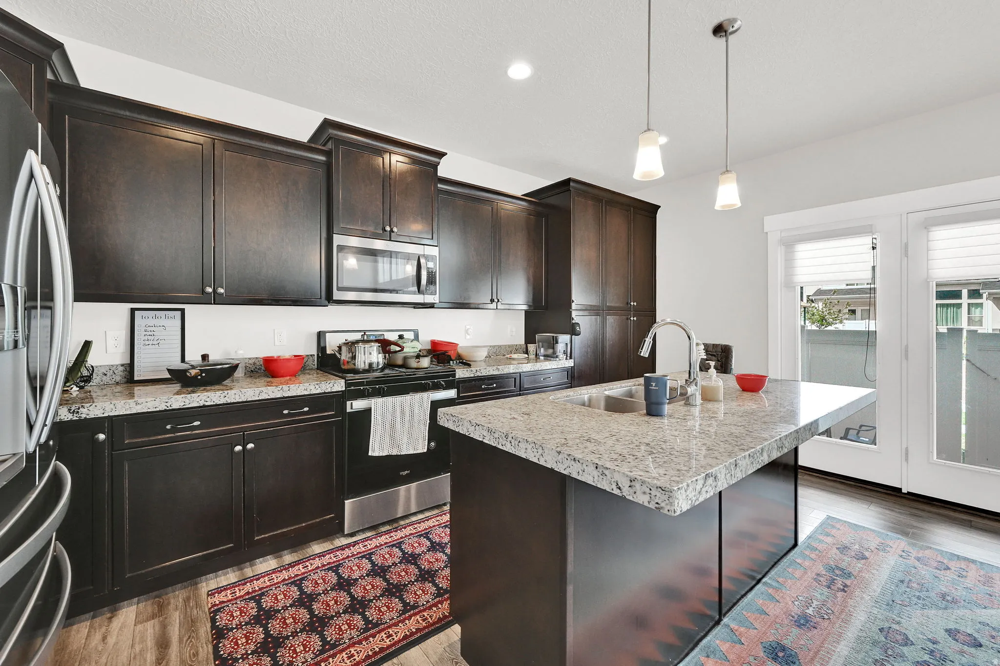 Kitchen with stainless steel appliances, a center island with sink, light countertops, light wood-style flooring, and pendant lighting