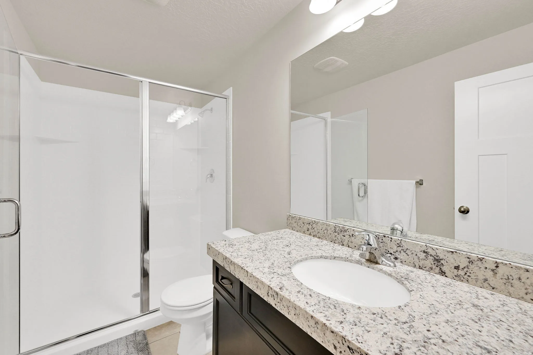 Full bath featuring a stall shower, vanity, a textured ceiling, and light tile patterned flooring