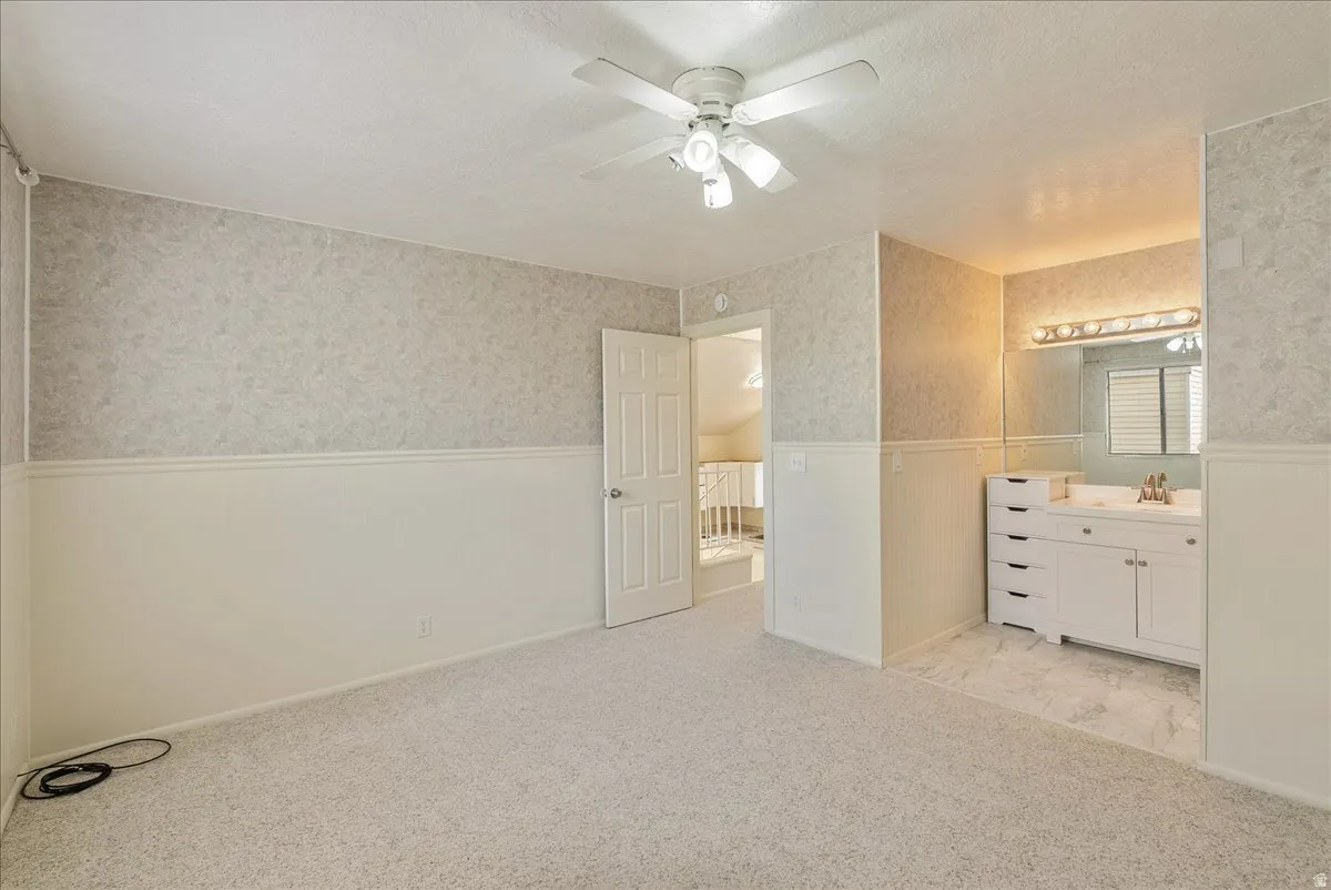 Unfurnished bedroom with wainscoting, a textured ceiling, wallpapered walls, light colored carpet, and a ceiling fan
