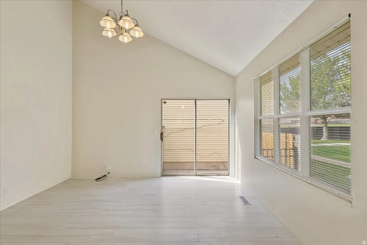 Spare room with vaulted ceiling, hanging lights, and light wood-type flooring