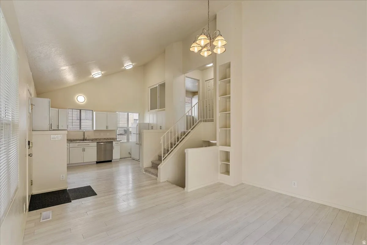 Kitchen with white cabinetry, built in shelves, stainless steel dishwasher, lofted ceiling, and hanging lights