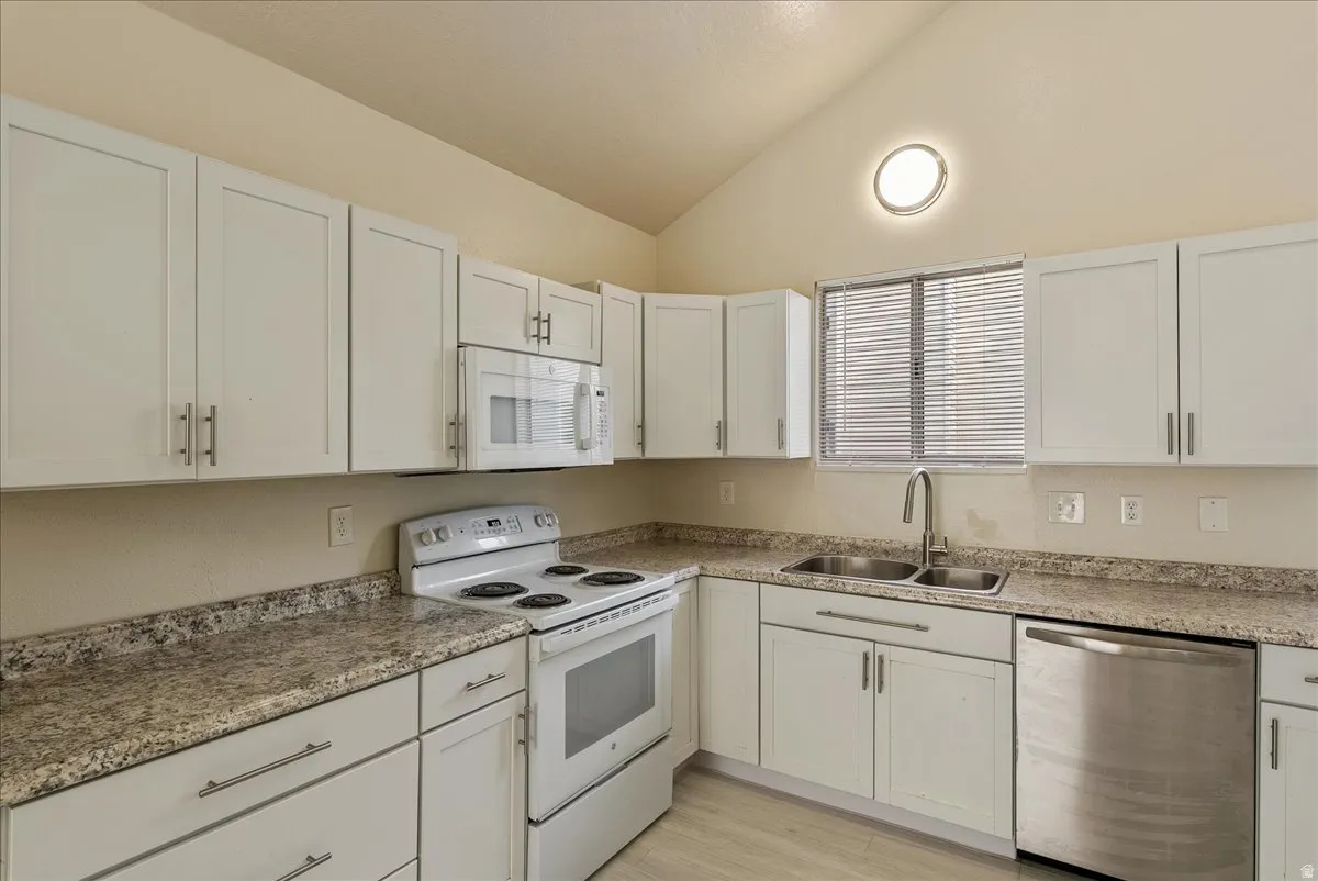 Kitchen with white appliances, white cabinetry, vaulted ceiling, and light wood-style flooring