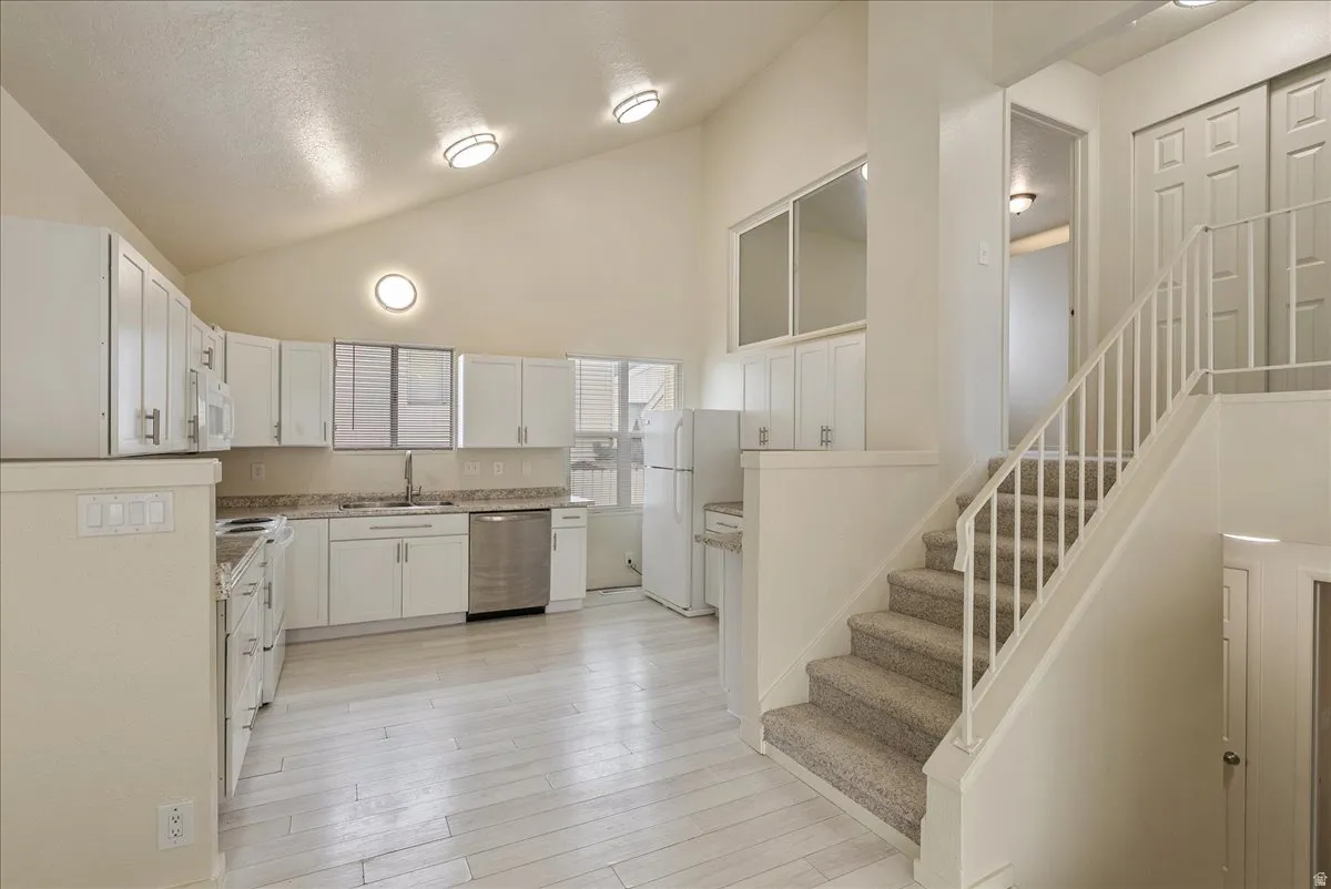 Kitchen featuring white cabinets, white appliances, light wood-style flooring, light stone counters, and a high textured ceiling