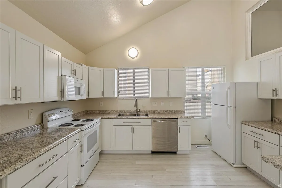 Kitchen featuring white appliances, white cabinetry, vaulted ceiling, and light wood finished floors