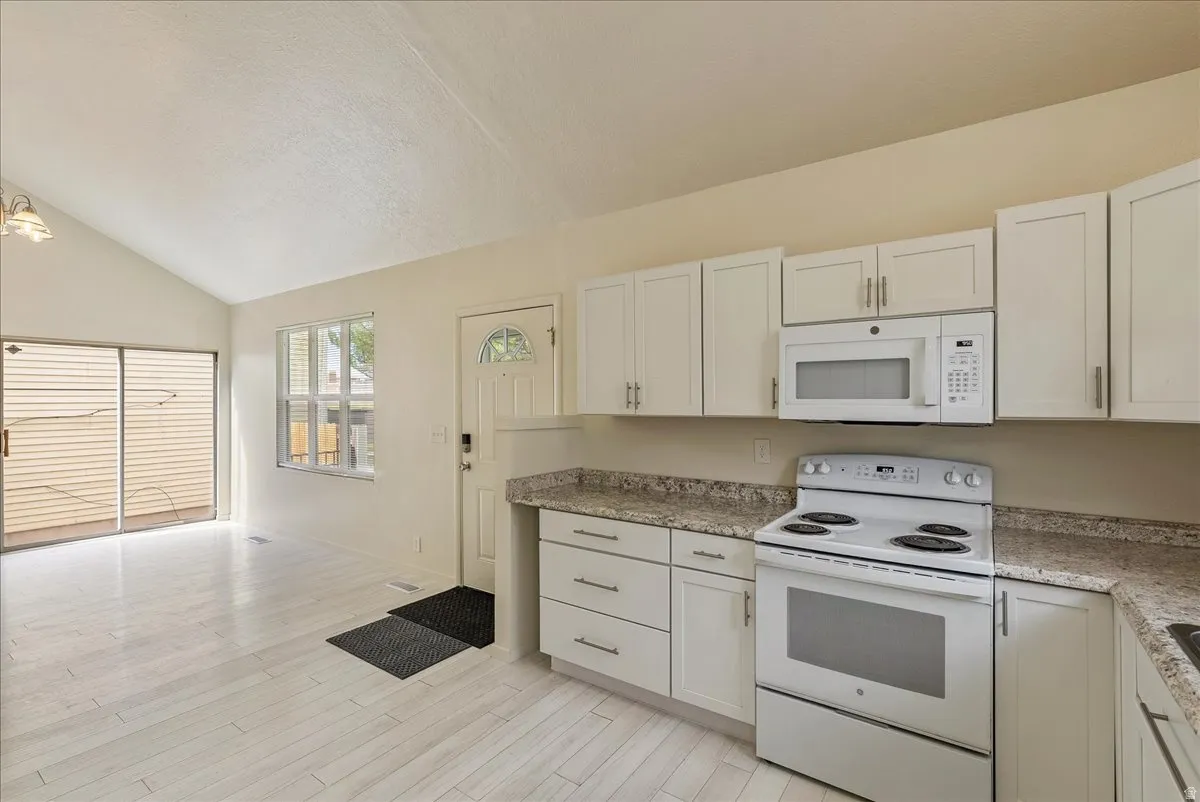 Kitchen with white appliances, vaulted ceiling, white cabinetry, and light wood-style floors