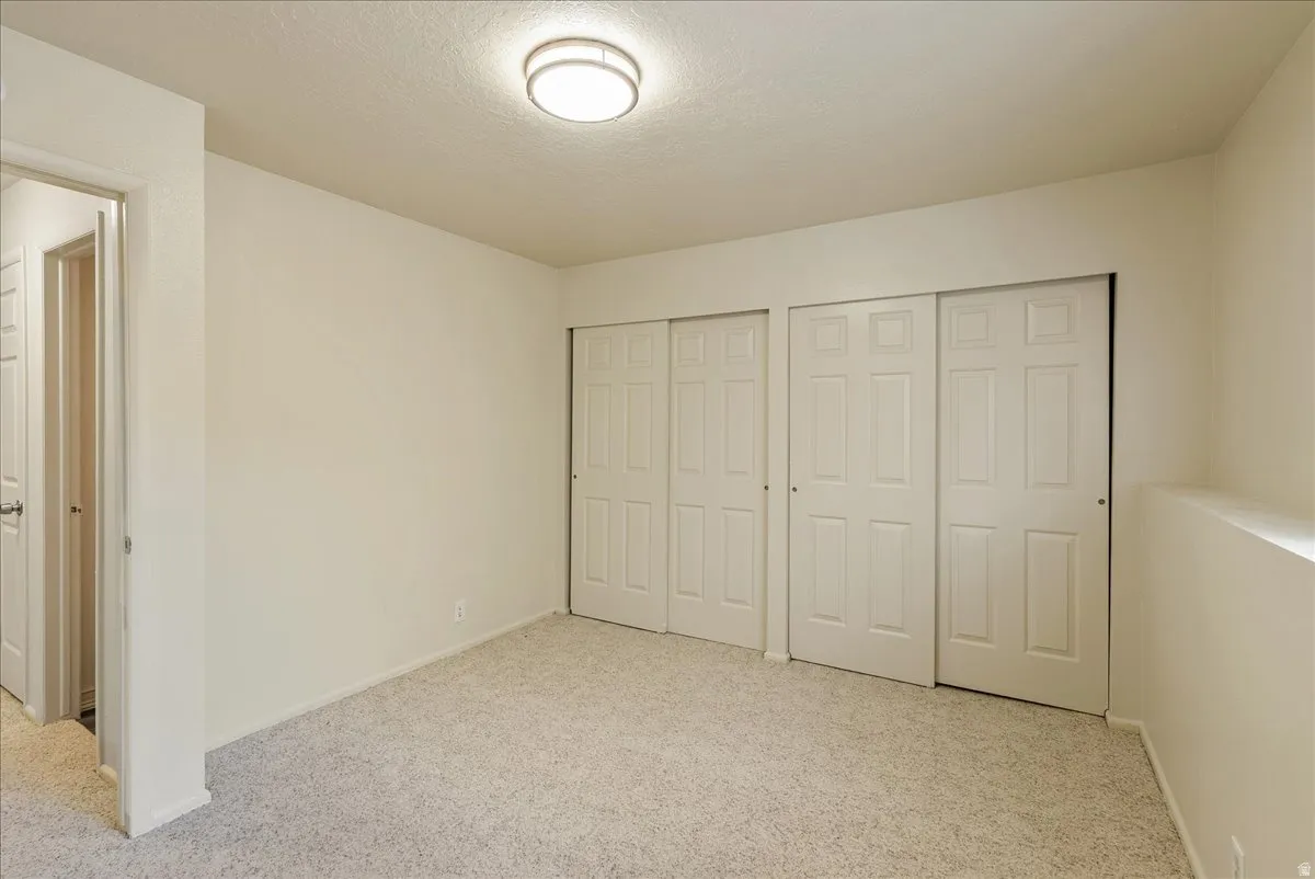 Unfurnished bedroom with multiple closets, light carpet, and a textured ceiling