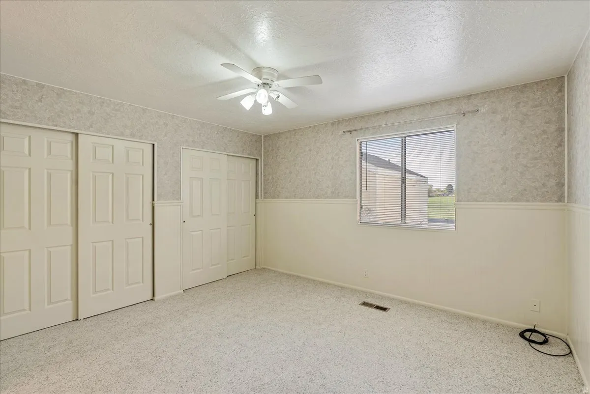 Unfurnished bedroom featuring a wainscoted wall, wallpapered walls, a textured ceiling, two closets, and carpet floors