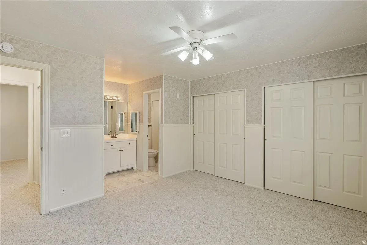 Unfurnished bedroom with a textured ceiling, a wainscoted wall, multiple closets, wallpapered walls, and light carpet