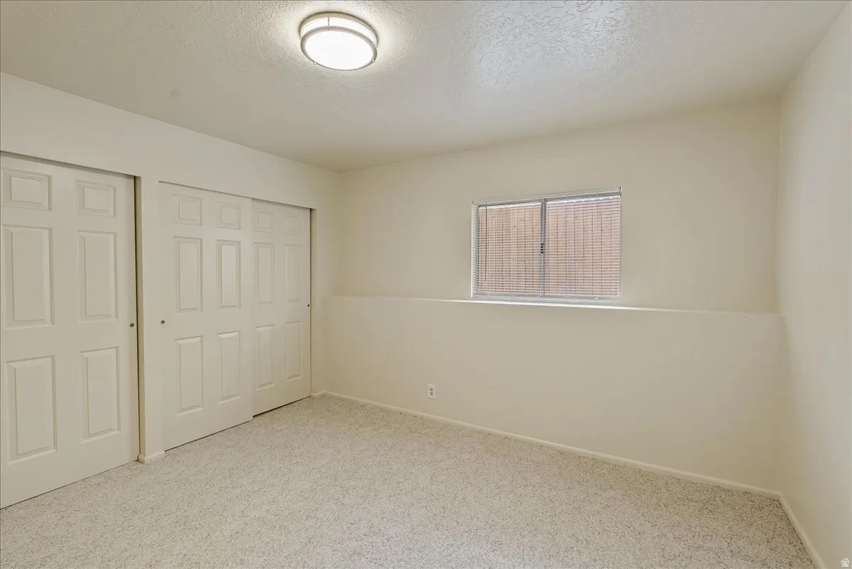 Unfurnished bedroom featuring a textured ceiling, light colored carpet, and multiple closets