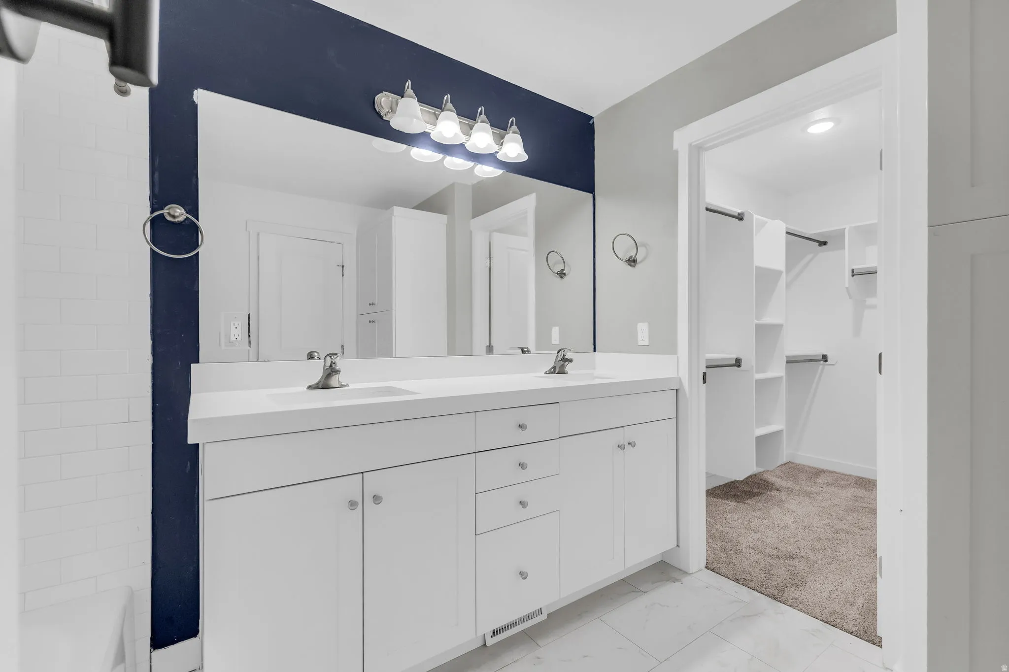 Bathroom featuring double vanity, light carpet, light marble finish flooring, and a walk in closet