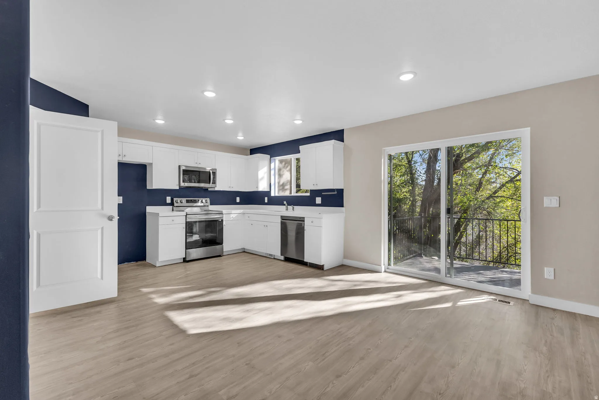 Kitchen with light countertops, stainless steel appliances, light wood-type flooring, white cabinetry, and recessed lighting