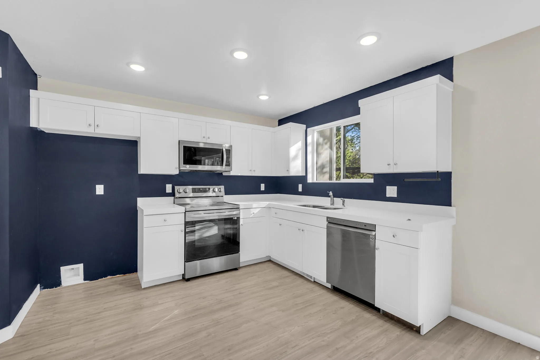 Kitchen featuring stainless steel appliances, white cabinetry, light countertops, light wood-type flooring, and recessed lighting