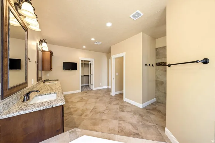 Full bath featuring double vanity, a walk in closet, and recessed lighting