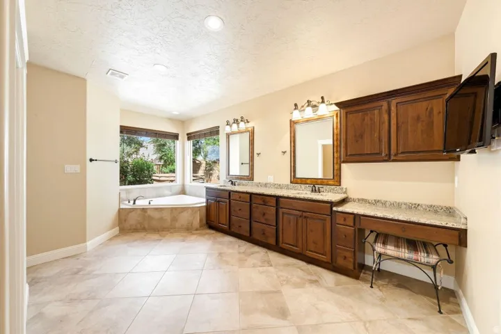 Full bath with double vanity, a textured ceiling, a garden tub, and recessed lighting